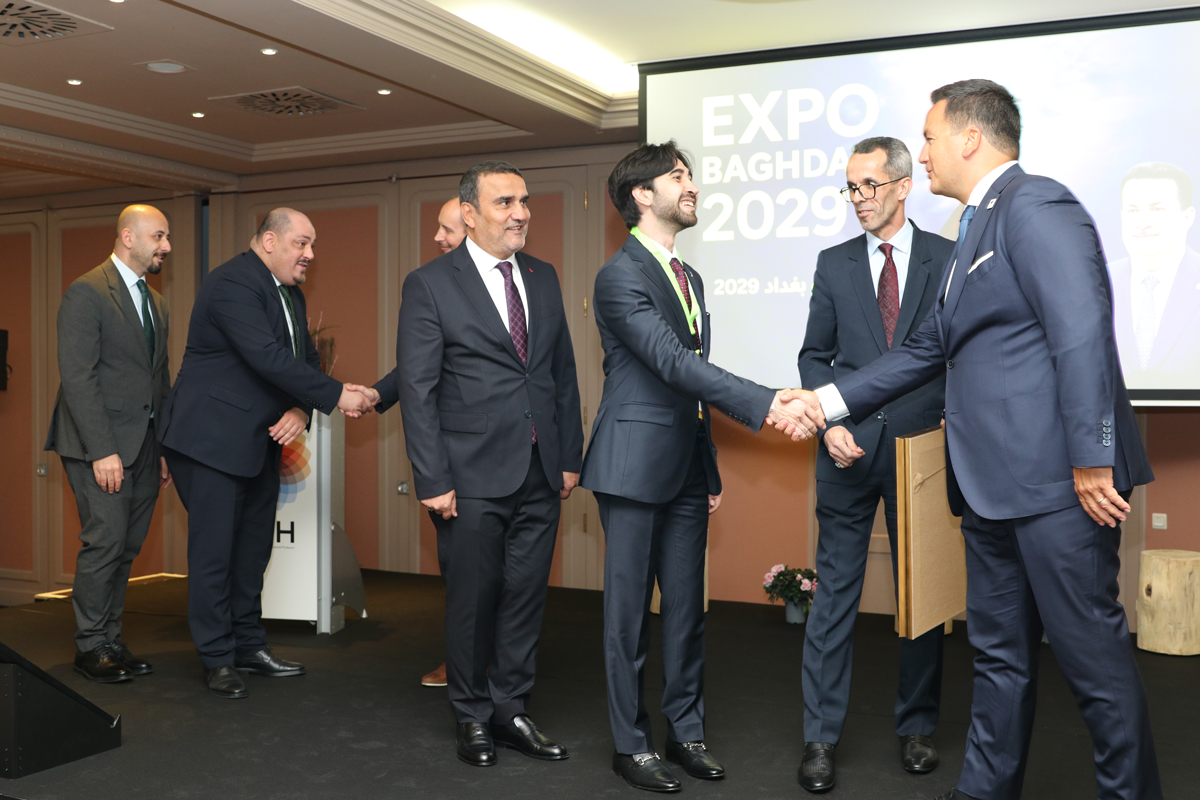 AIPH President shakes hands with the CEO of Expo 2029 Baghdad on stage, joined by Iraqi diplomats and representatives following the approval ceremony