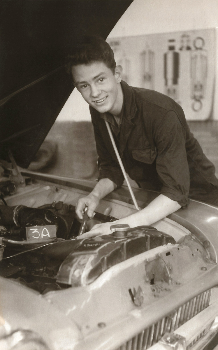 Young Jan Roelofs is working as a mechanic under a car bonnet in a workshop.