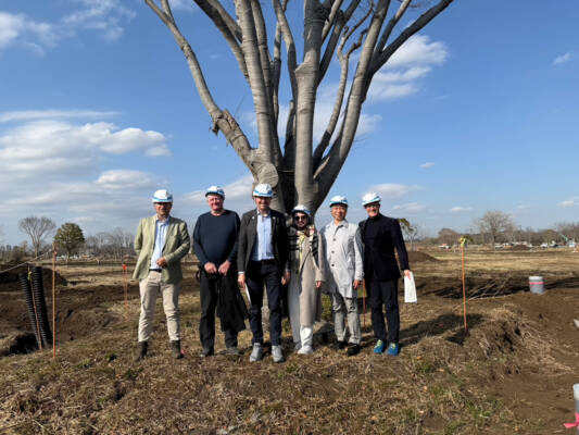 AIPH delegation visiting GREEN×EXPO 2027 site beside mature tree and early landscape works