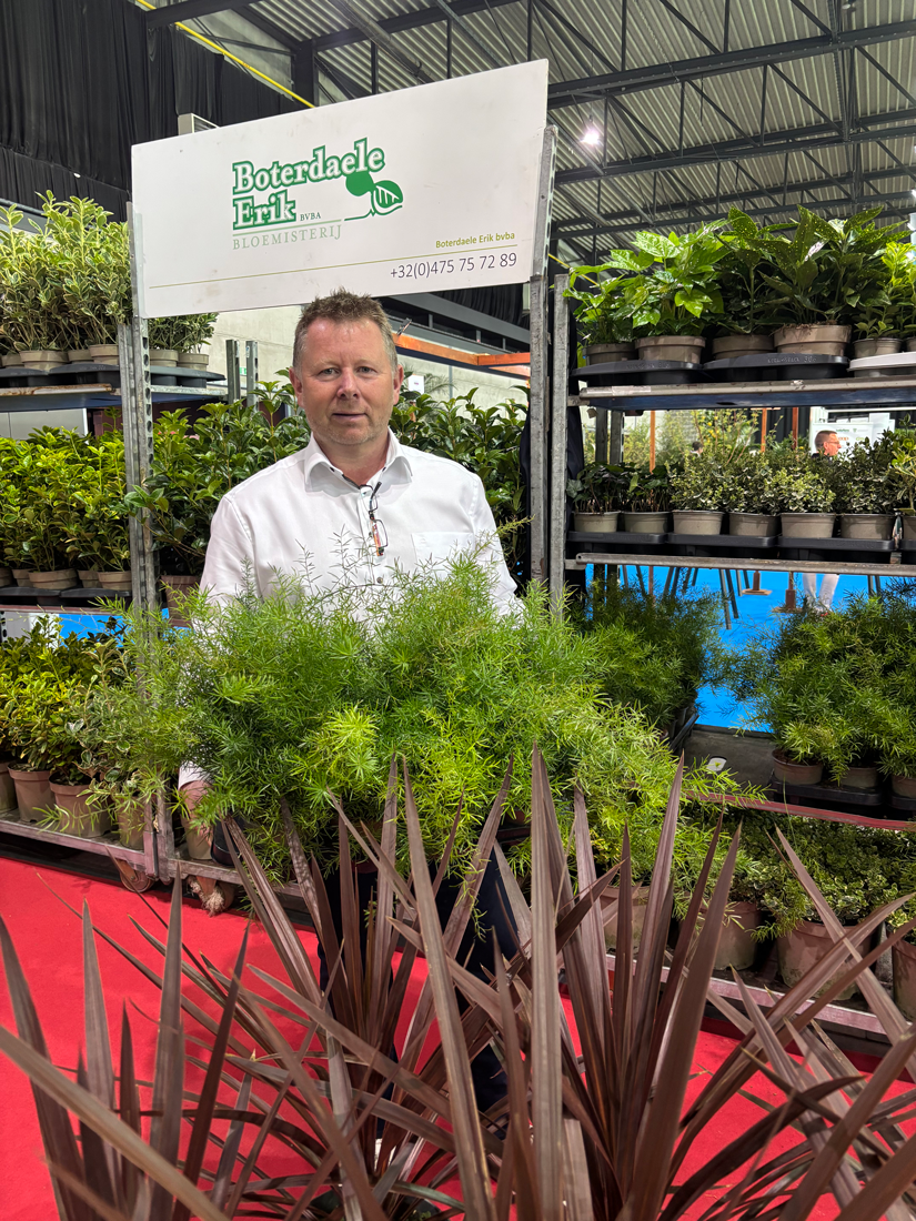 Erik Boterdaele standing at his plant display stand at Florall, surrounded by evergreen shrubs.
