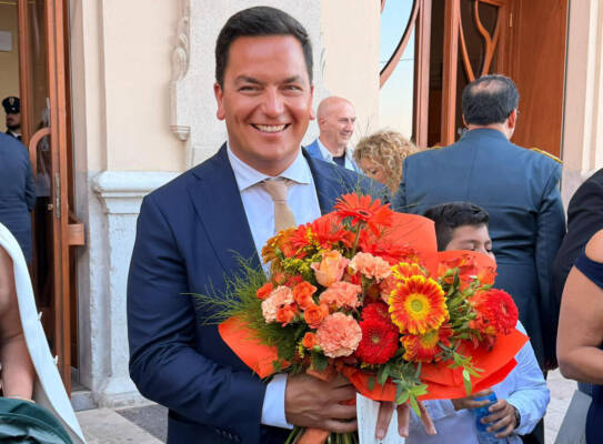 Leonardo Capitanio smiles while holding flowers and his Cavaliere certificate outside the ceremony venue.
