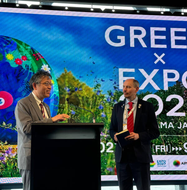 Speaker at a podium in front of a GREEN×EXPO 2027 Yokohama presentation screen during an AIPH meeting.