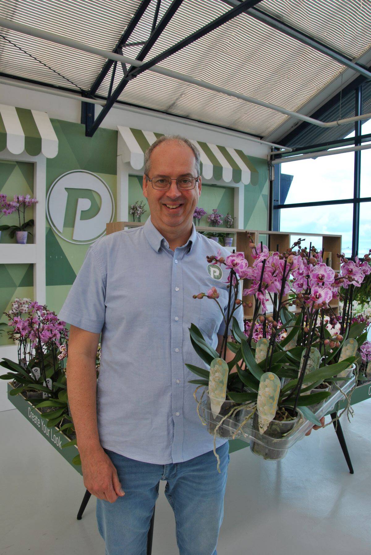 Patrick van der Arend holding a tray of potted Phalaenopsis orchids.