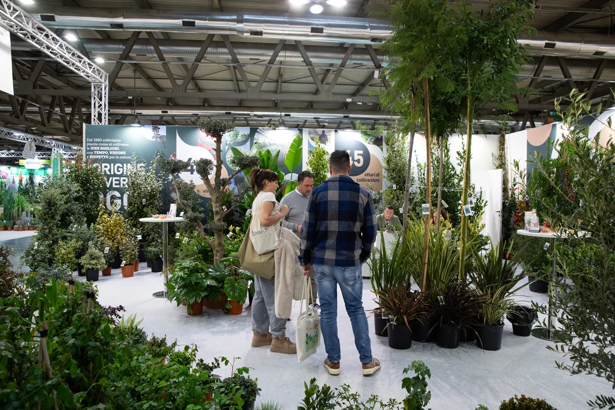 Visitors discussing plant selections at nursery exhibitor stand in Milan.